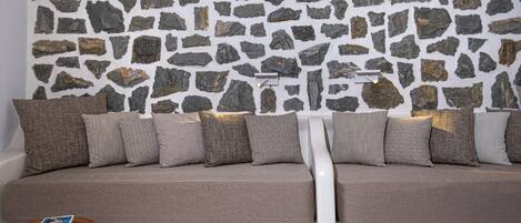 A modern living room with a stone wall, a beige sofa with patterned cushions, and a small wooden side table with a book.