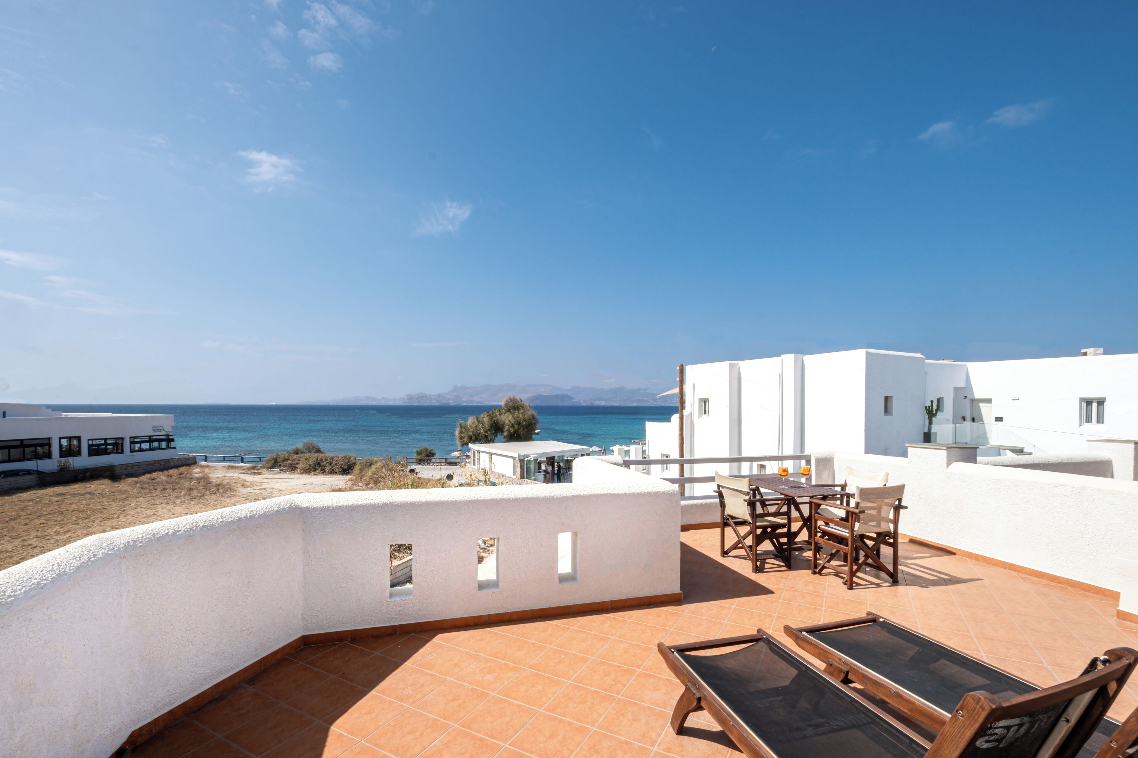 A rooftop terrace with a view of the sea, a table with chairs, and a pool table.