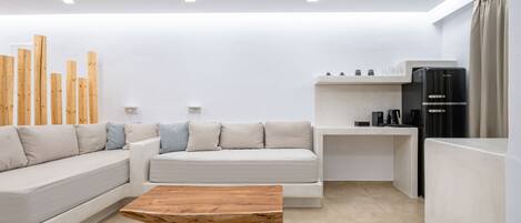 A modern living room with a sectional sofa, a wooden coffee table, a built-in kitchen area with a black refrigerator, and a minimalist design.