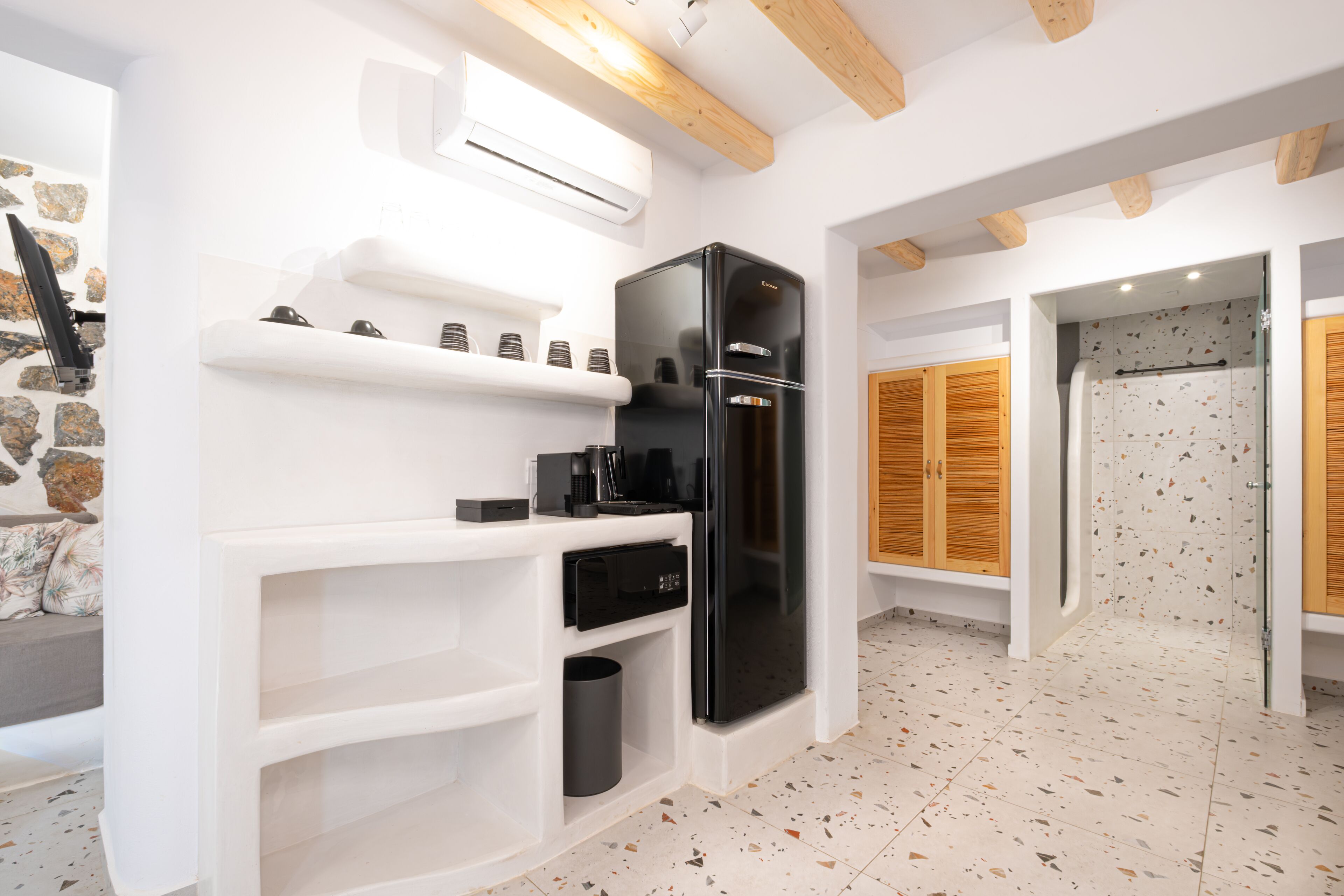 A modern kitchen with a black refrigerator, white cabinetry, and a stone wall.