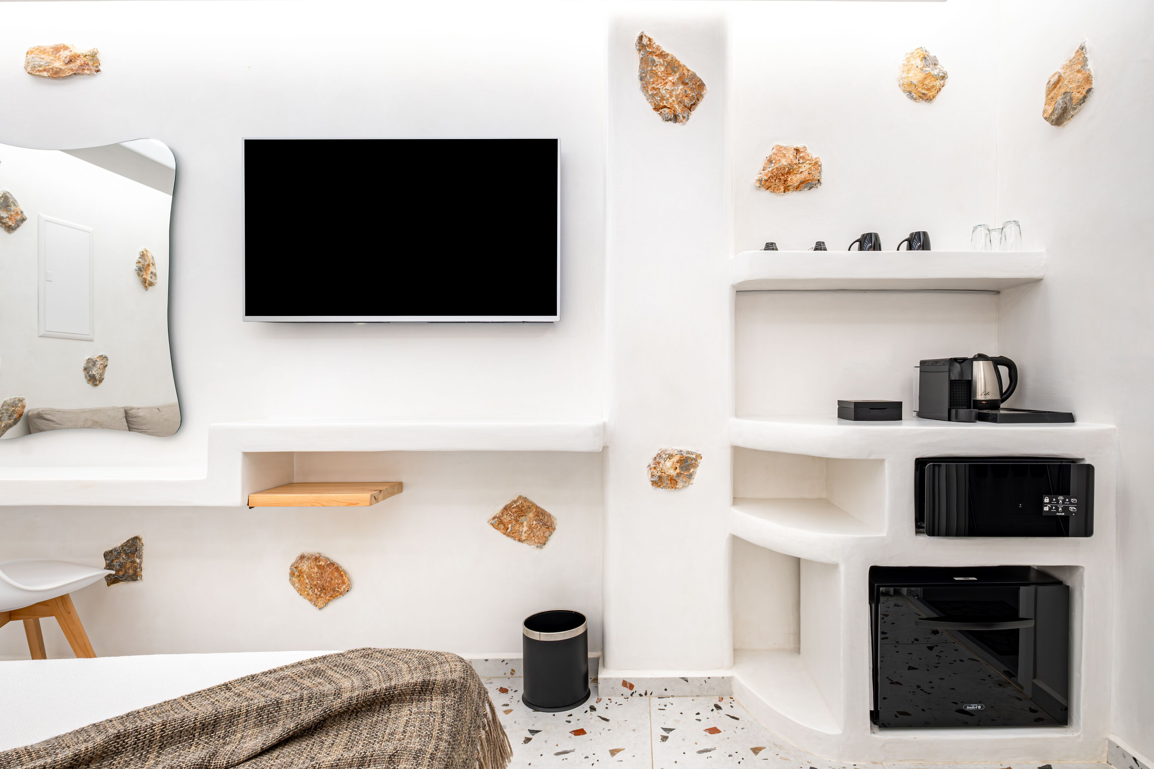 Ein modernes Zimmer mit Flachbildfernseher, Regalen, einer Kaffeemaschine und einem Mülleimer.