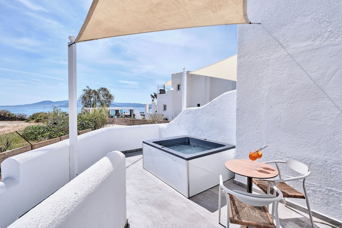 A balcony with a hot tub, white furniture, and a view of the sea and buildings.