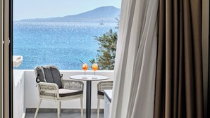 A balcony with a view of the sea, two drinks on a table, and a chair.