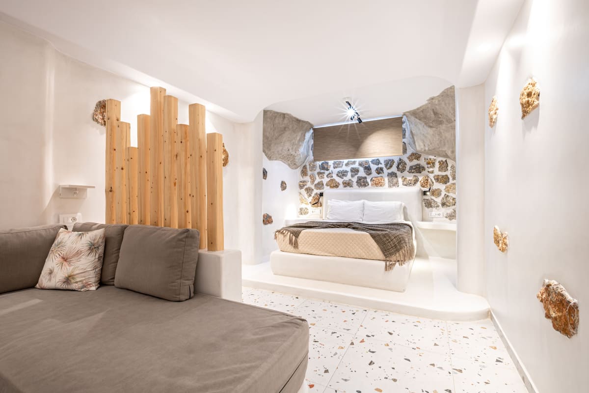 A modern bedroom with a large bed, a sofa, and a bathroom with a stone wall and bathtub.