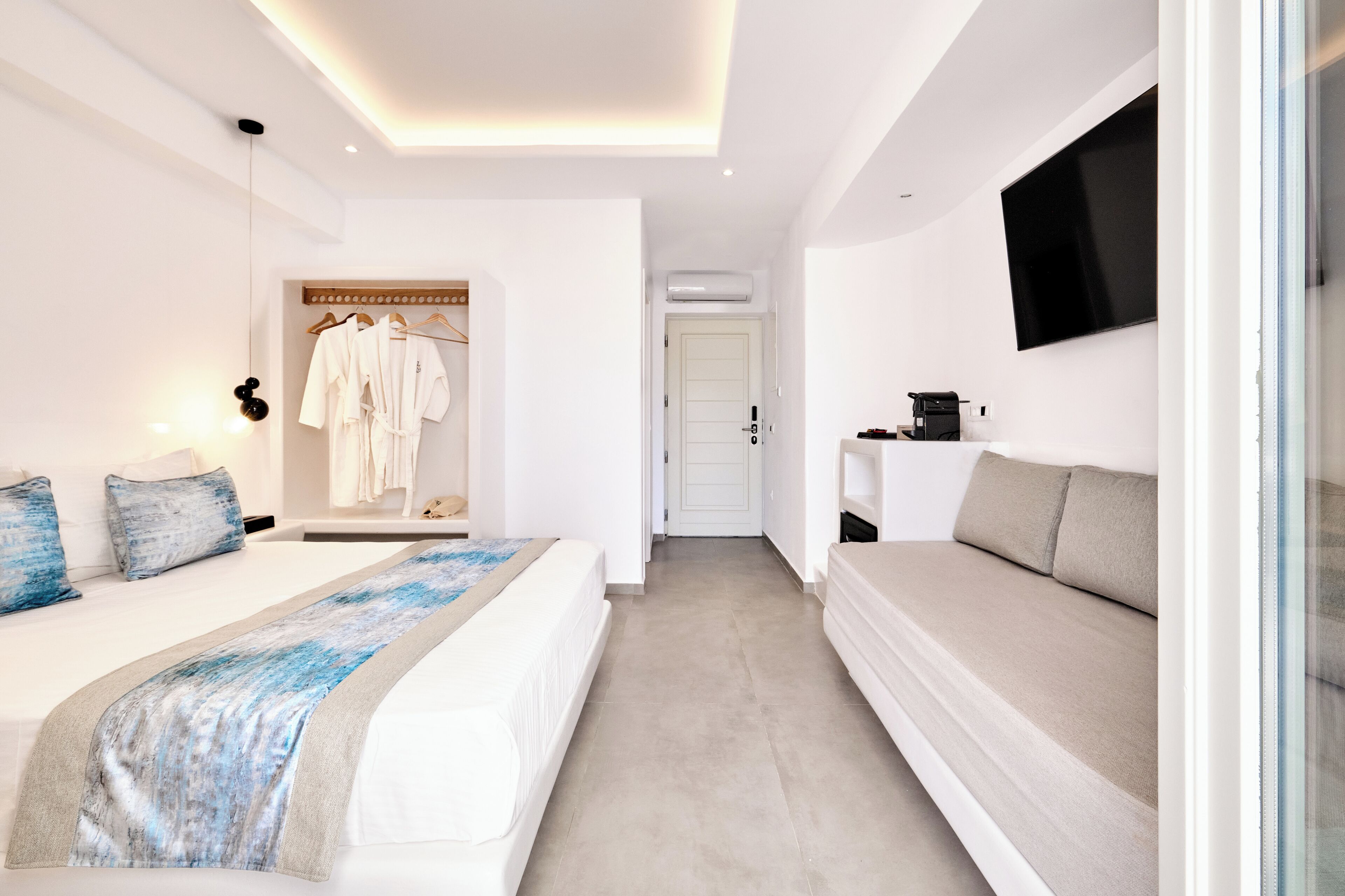 Una habitación de hotel moderna con una cama, un sofá, un televisor y un armario.