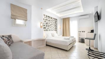A modern hotel room with a bed, a sofa, a desk, and a stone wall.