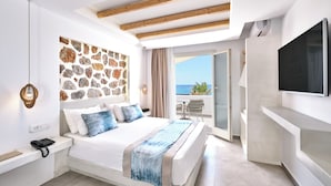 A bedroom with a stone wall, a bed with blue pillows, a TV, and a balcony with a view.