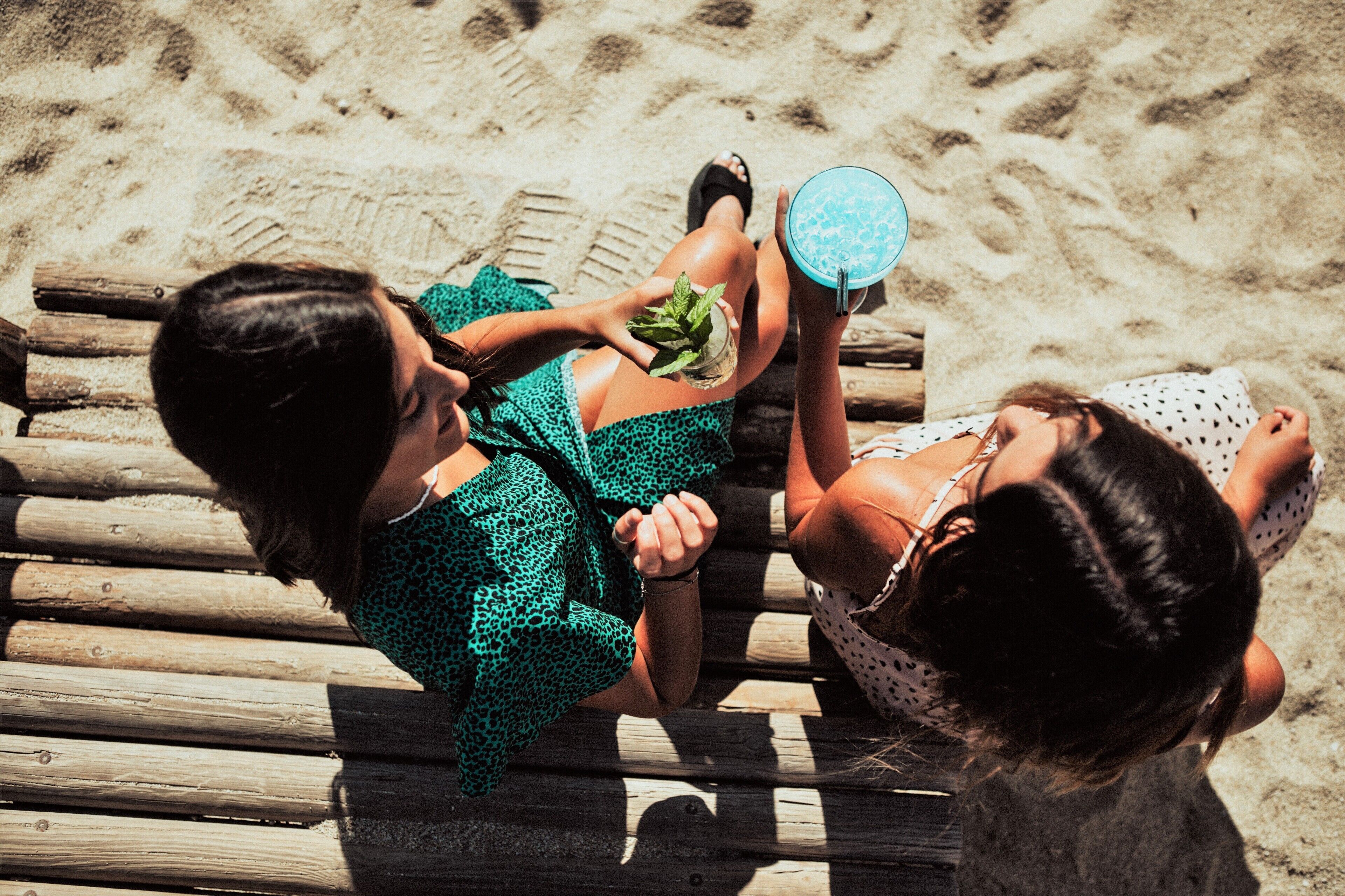 Two people sitting on a wooden bench on a sandy beach.