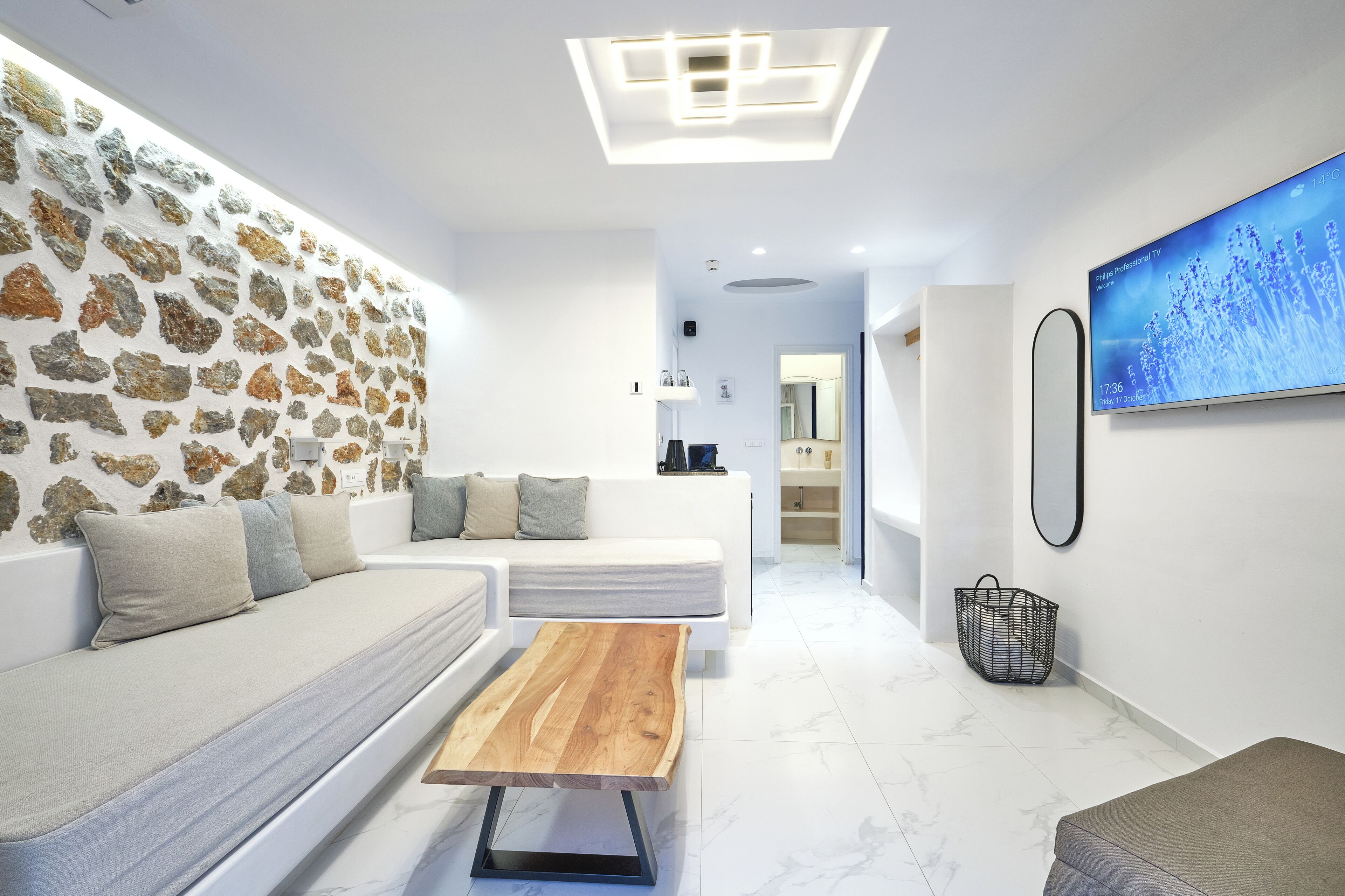 Een moderne woonkamer met een stenen muur, een witte bank, een houten salontafel en een televisie waarop een natuurlandschap te zien is.