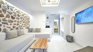 Een moderne woonkamer met een stenen muur, een witte bank, een houten salontafel en een televisie waarop een natuurlandschap te zien is.