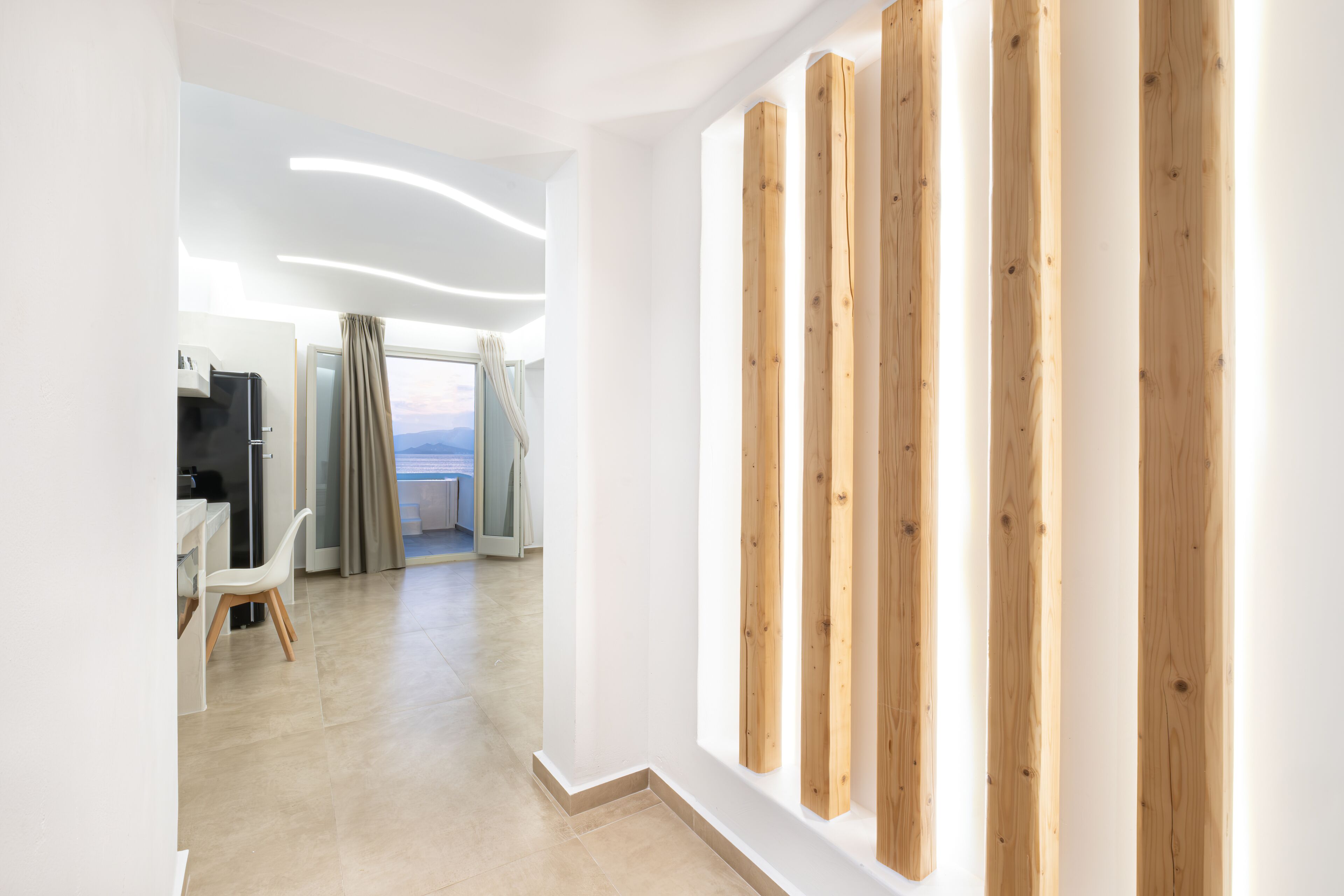 A modern hotel room with a view, a wooden accent wall, and a dining area with a chair.
