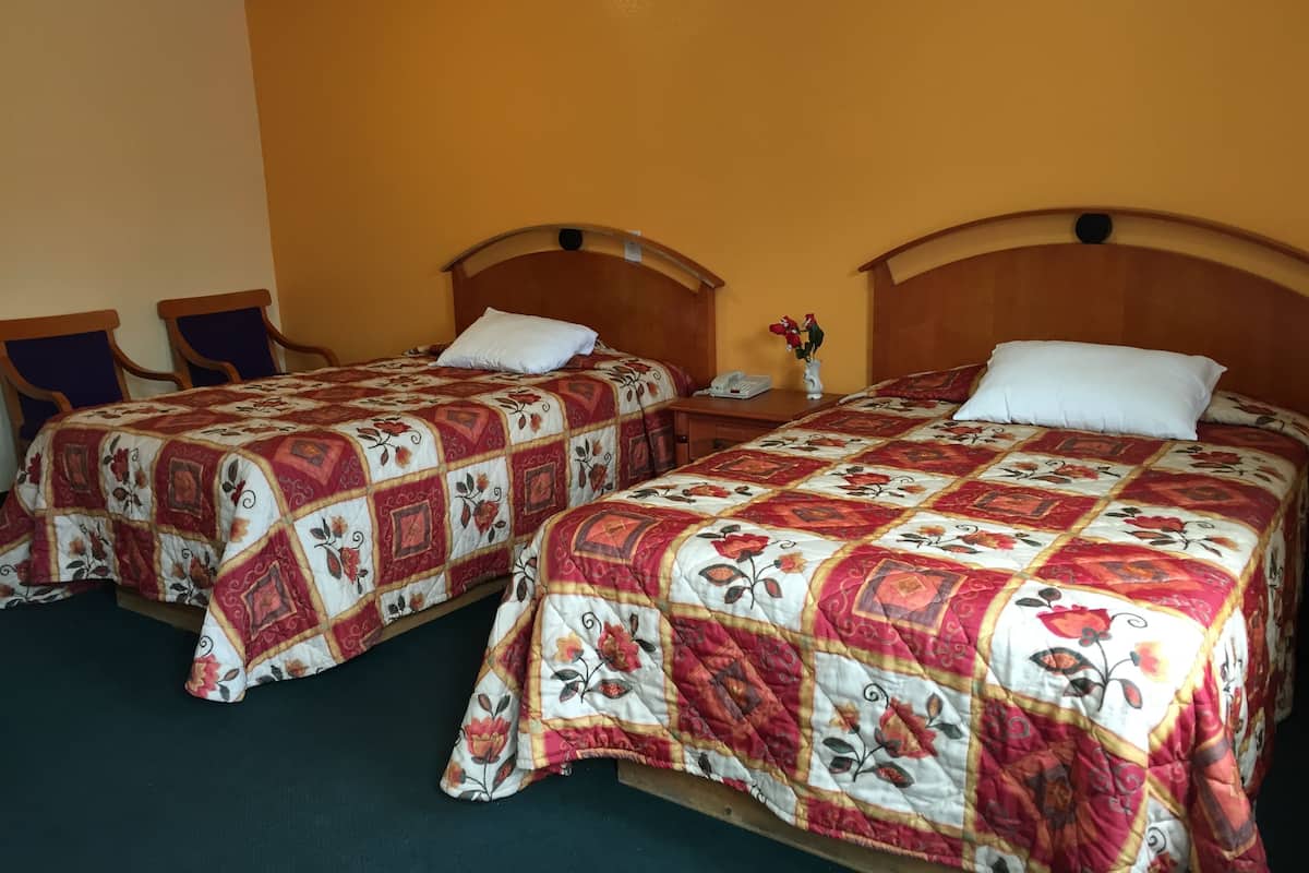 Two double beds with floral-patterned bedding, wooden headboards, and a nightstand with a phone and vase between them.