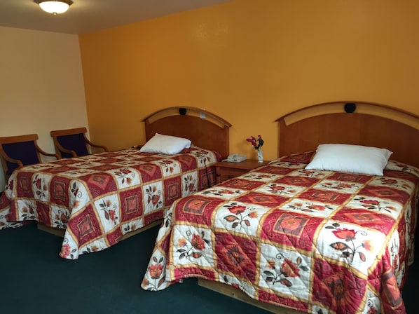 Dos camas dobles con ropa de cama de estampado floral, cabeceros de madera y una mesita de noche con un teléfono y un florero entre ellas.