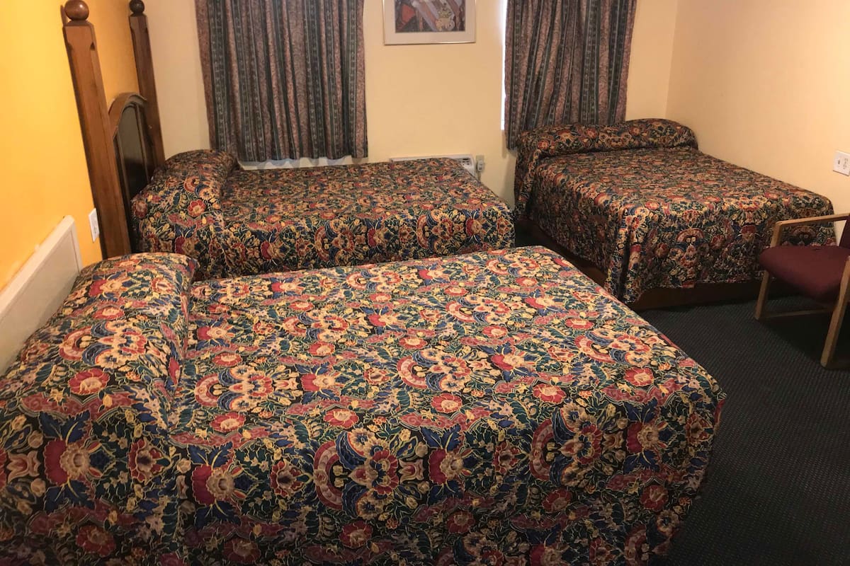A hotel room with two single beds, a wooden headboard, a chair, and a framed picture on the wall.