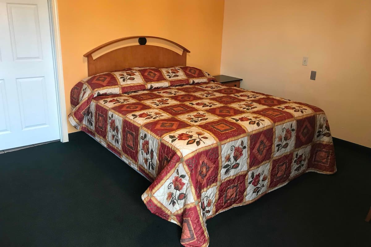 A single bed with a floral-patterned bedspread and matching pillows in a room with a plain wall and a white door.