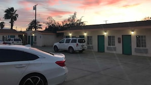 Un edificio con varias habitaciones, cada una con puerta y ventanas, y un estacionamiento con coches.