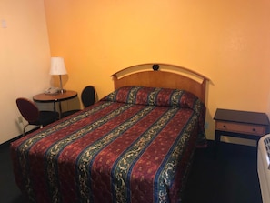 Una habitación de hotel con cama, escritorio, silla y mesita de noche.
