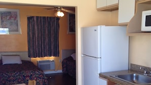 Una habitación de hotel funcional con cama, kitchenette pequeña, zona de comedor y baño.