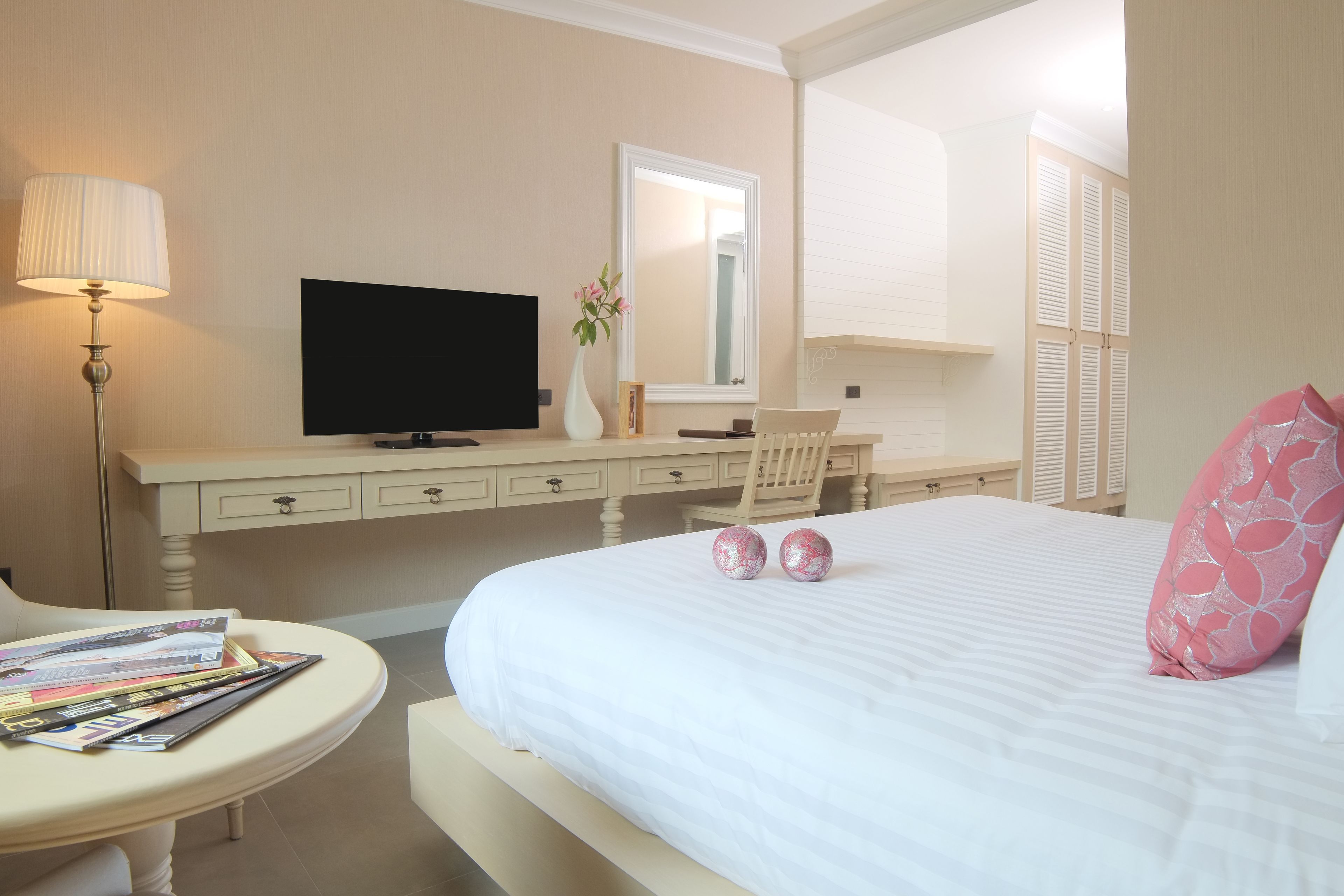 A hotel bedroom with a bed, a TV, a desk, a chair, and a table with magazines.
