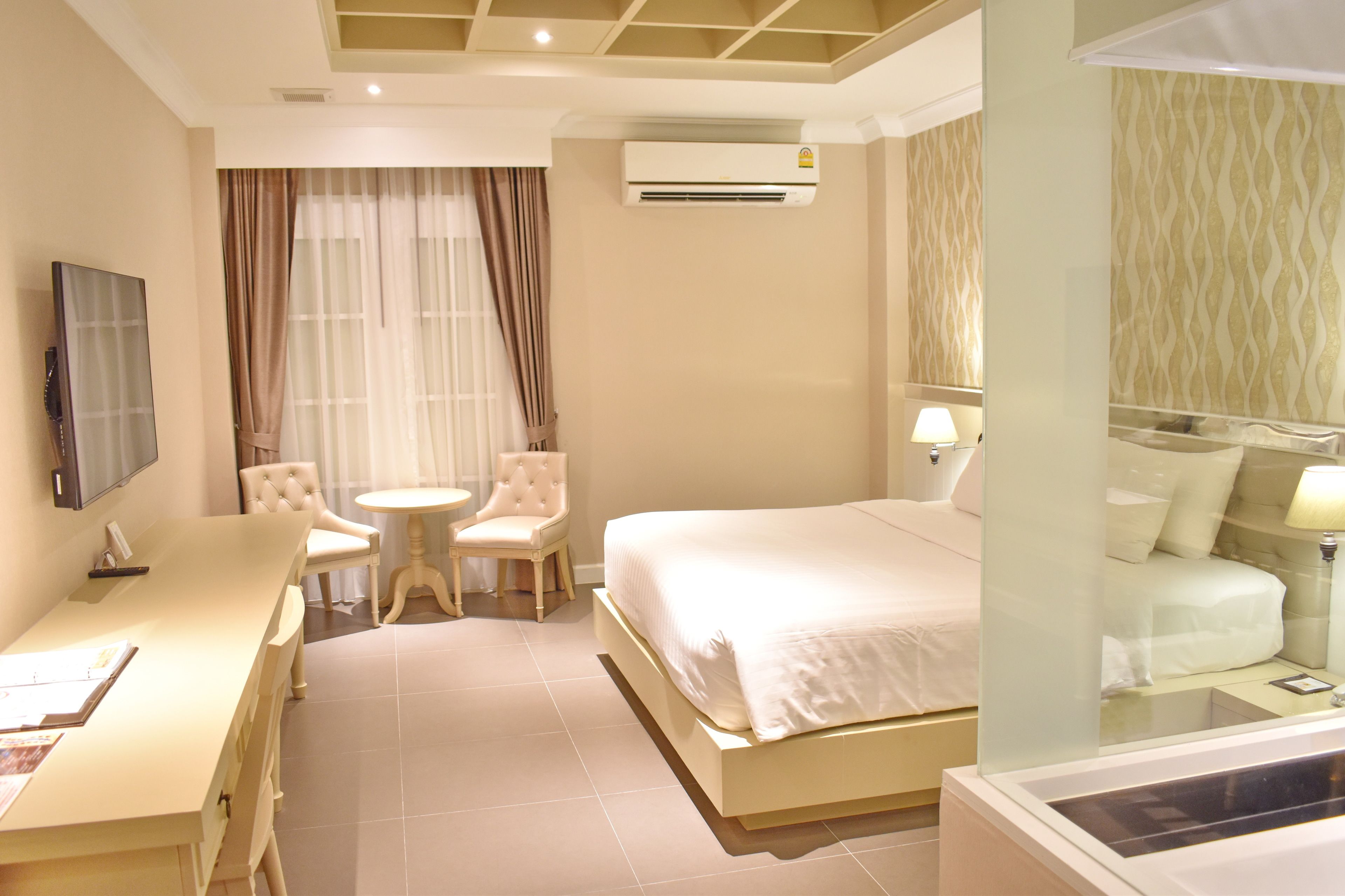 A hotel room with a bed, a desk, a chair, a small table, an air conditioning unit, and a window with curtains.
