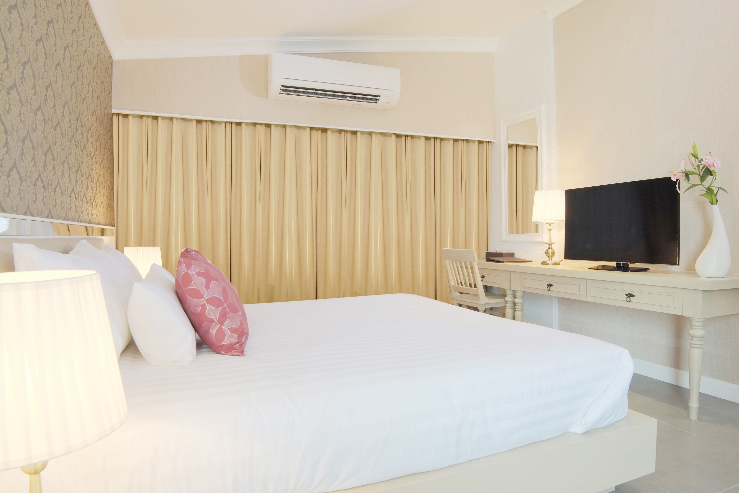 A hotel room with a bed, a desk, a television, and an air conditioning unit.