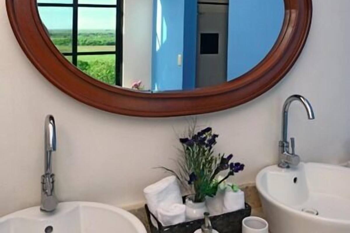 Une salle de bain avec deux lavabos, un grand miroir et une fenêtre donnant sur un paysage verdoyant.