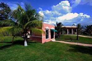 Un bâtiment rose surmonté d’un auvent vert, entouré de palmiers et d’une pelouse bien entretenue.
