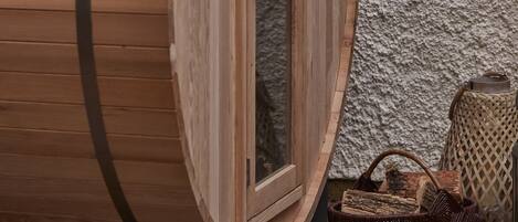 Une fenêtre en forme de tonneau en bois, avec une porte, un banc en bois et un panier en osier posé sur le sol.