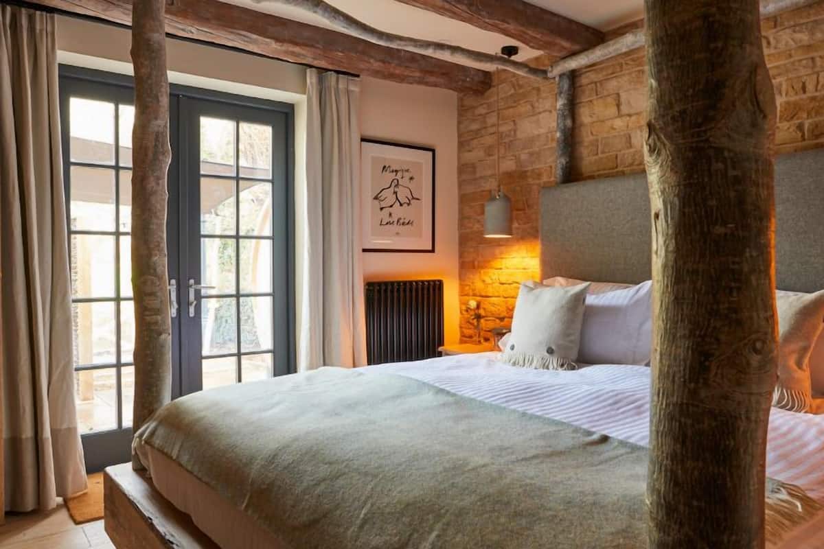 Une chambre à coucher avec un grand lit, un mur en pierre, une fenêtre avec des rideaux et un tableau encadré accroché au mur.