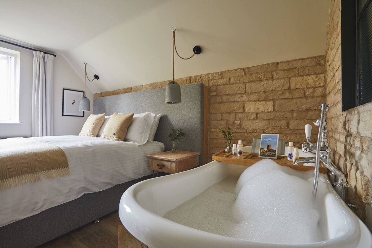 Une chambre avec un grand lit, une table de chevet en bois, une baignoire blanche et un mur en pierre.