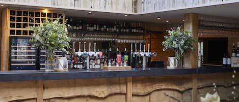 Zona de bar con paneles de madera, una estantería para vinos y una variedad de botellas y copas.