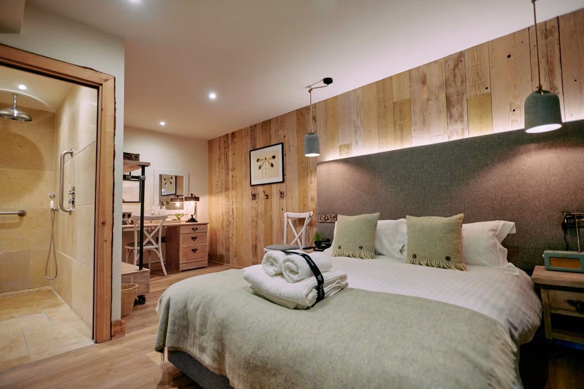 A hotel room with a bed, a desk, a chair, a shower, and a wooden wall.