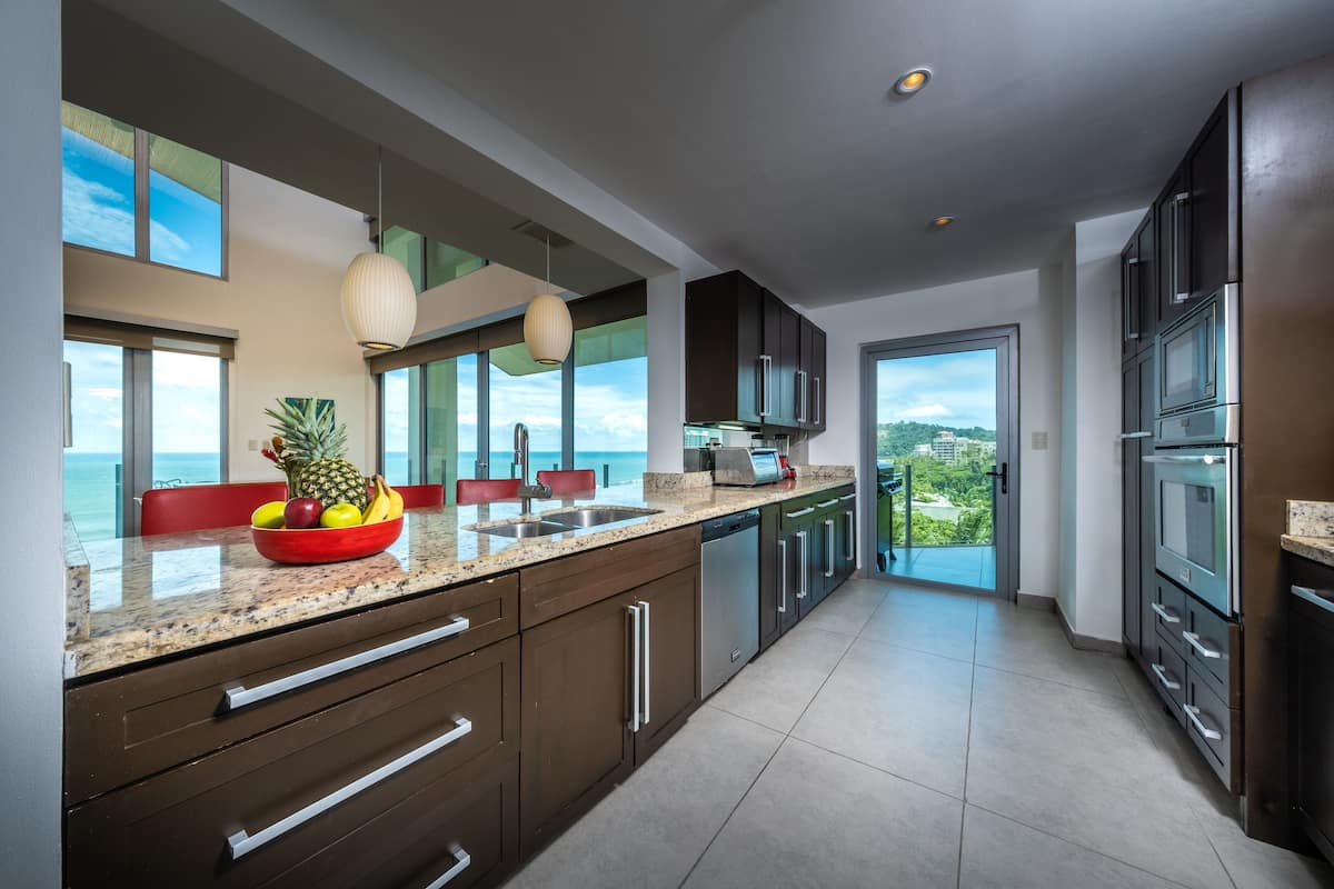 A modern kitchen with granite countertops, stainless steel appliances, and a large window overlooking a scenic view.