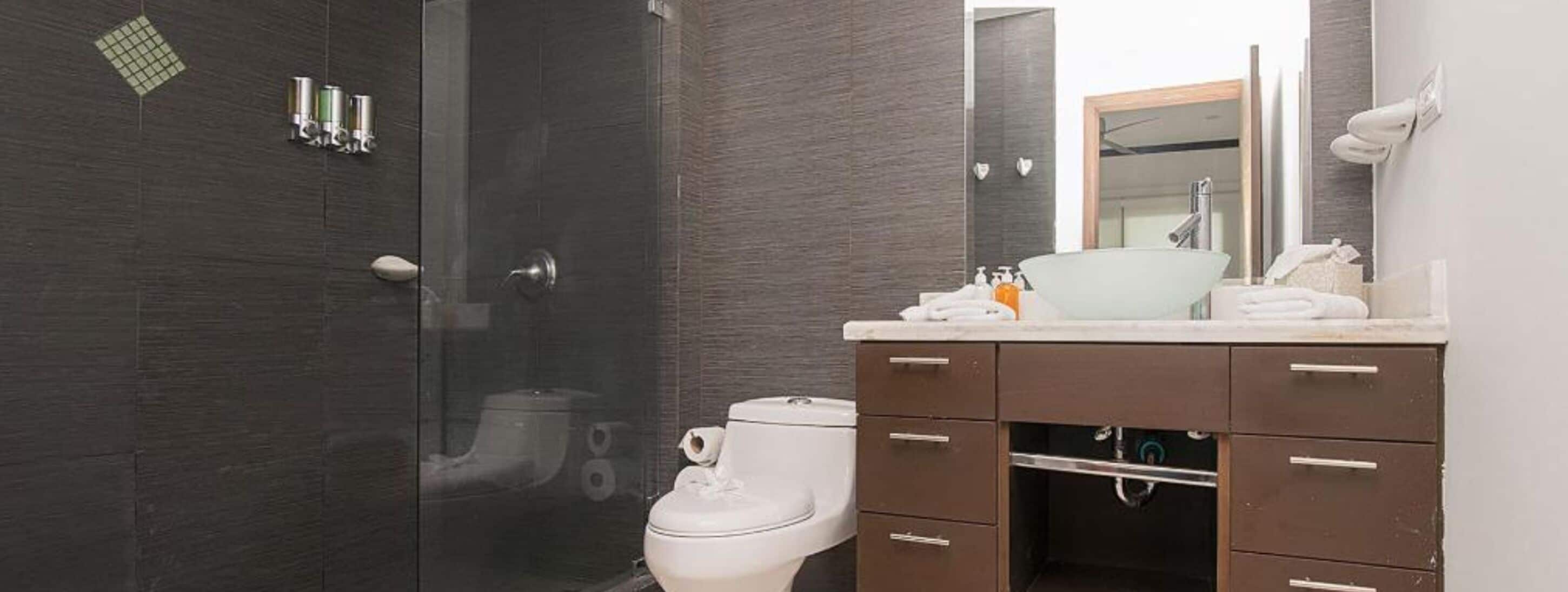 Ein modernes Badezimmer mit Glasdusche, weißer Toilette und Waschtisch mit Spiegel und Waschbecken.