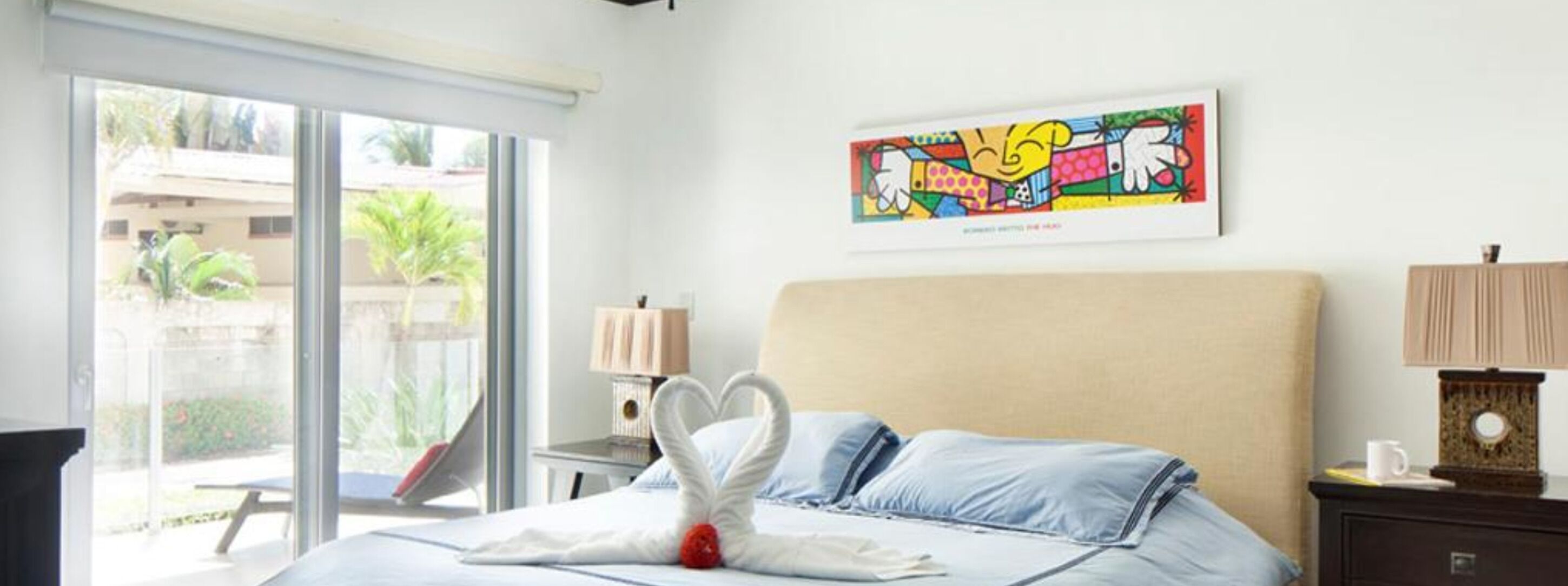 Une chambre d’hôtel comprenant un lit, une table de chevet, une lampe, une œuvre d’art murale et une vue sur l’extérieur.