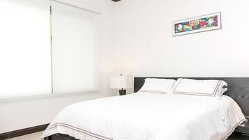 Ein Hotelzimmer mit einem großen Bett, zwei Nachttischlampen, einer grauen Bank und einem farbenfrohen Kunstwerk an der Wand.