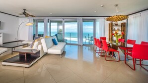 A modern living room with a sofa, coffee table, TV, and dining area with red chairs. - Best in Jaco Diamante del Sol Condos (Jacó)