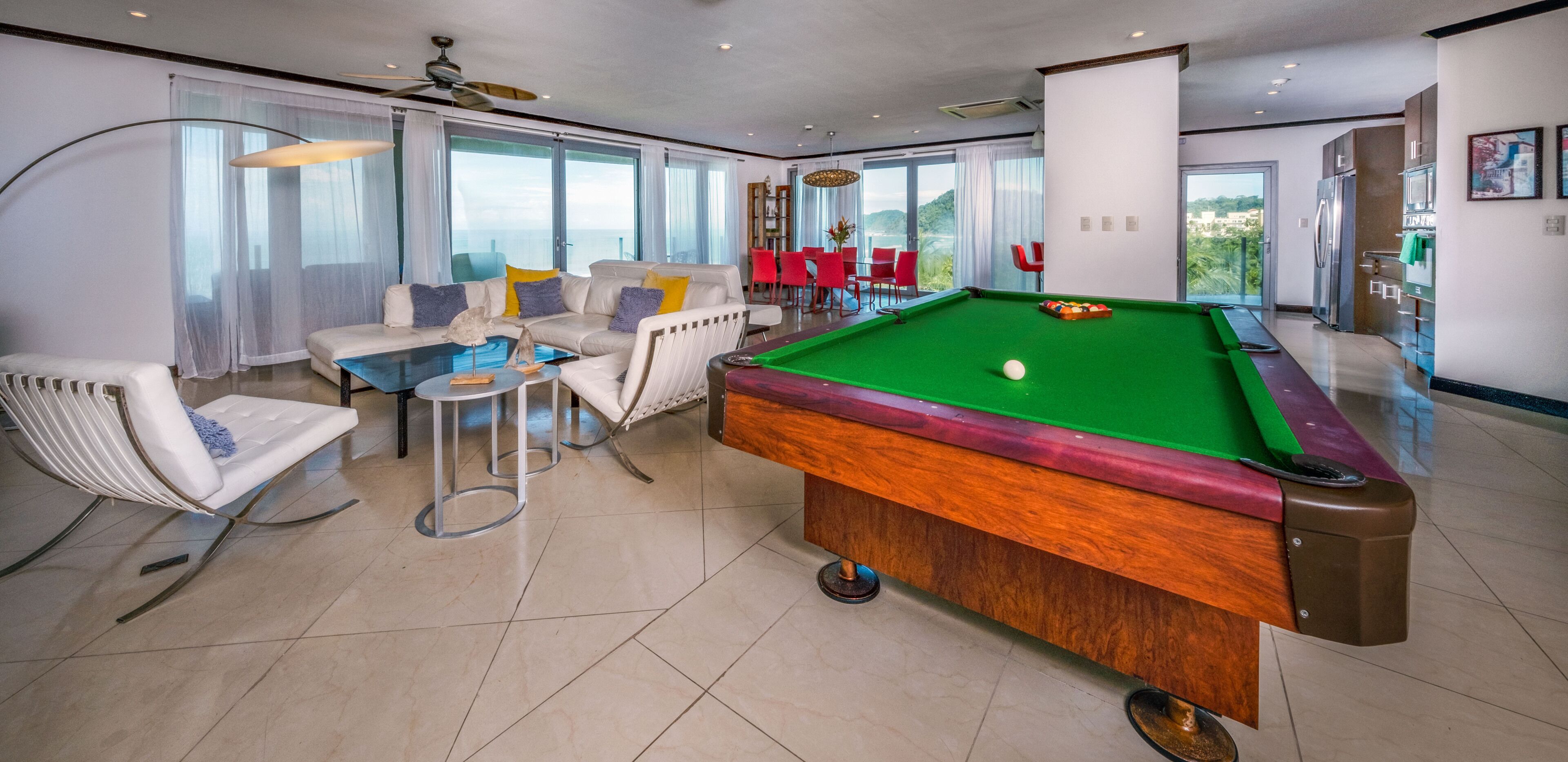 Een moderne woonkamer met een pooltafel, comfortabele zithoek en grote ramen met uitzicht op de omgeving.