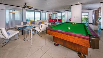 Een moderne woonkamer met een pooltafel, comfortabele zithoek en grote ramen met uitzicht op de omgeving.