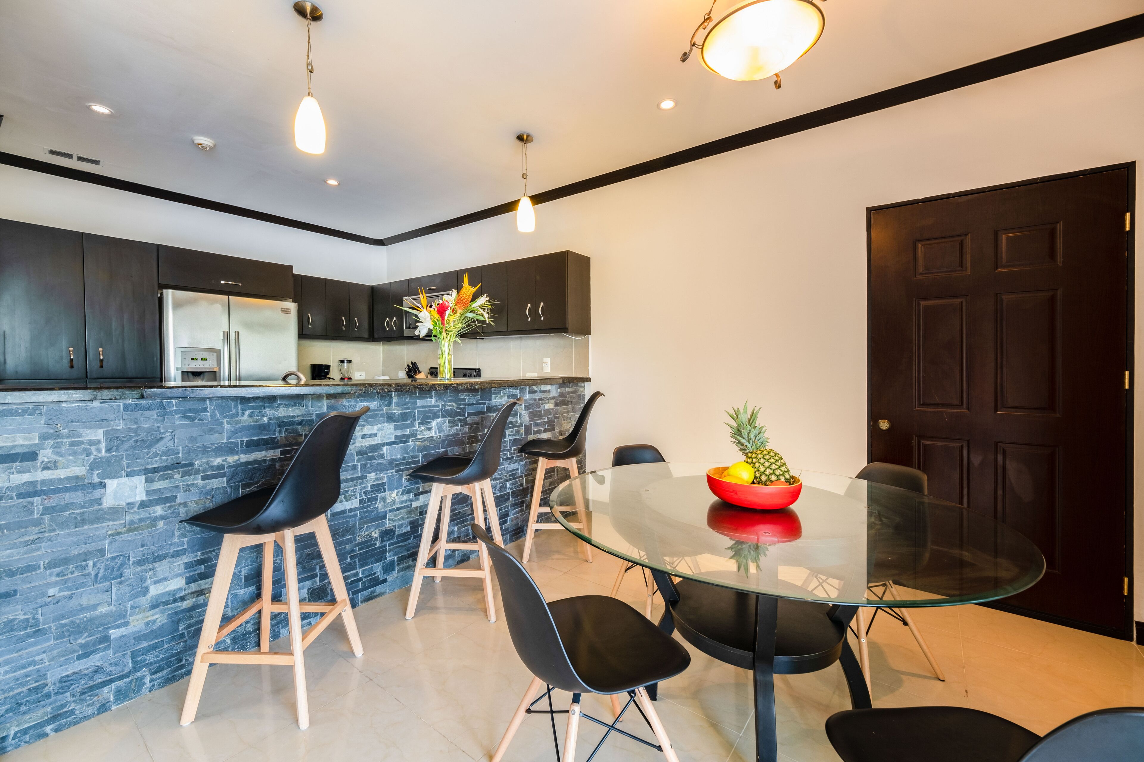 A modern kitchen with dark cabinets, a stainless steel refrigerator, and a glass island with bar stools.