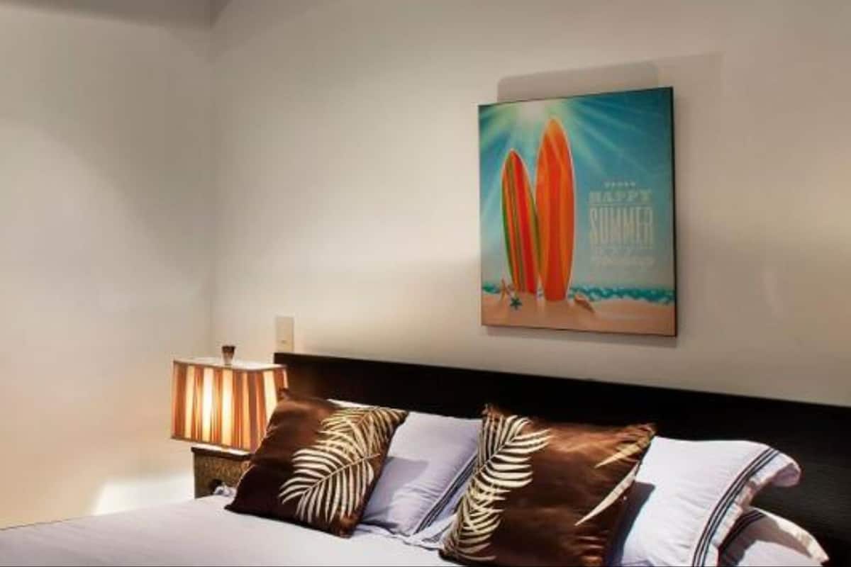 A hotel room with a bed, a nightstand, a lamp, and a painting on the wall.