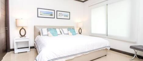 Un dormitorio con una cama grande, dos mesitas de noche con lámparas, un ventilador de techo y un ventanal amplio.