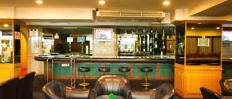 Eine Bar mit Ledersitzgelegenheiten, einer Theke mit Fernseher sowie verschiedenen Flaschen und Gläsern.