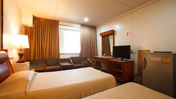 A hotel room with two beds, a desk with a television, a refrigerator, and a window with curtains.