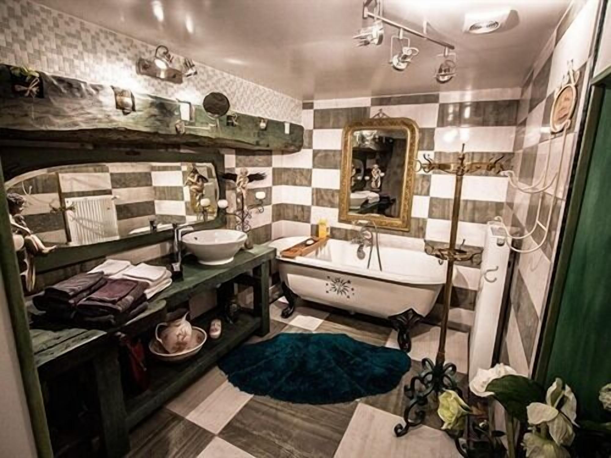 Een badkamer met een betegelde achterwand in ruitpatroon, een vrijstaand bad, een wastafelmeubel met spiegel, en een groene deur.