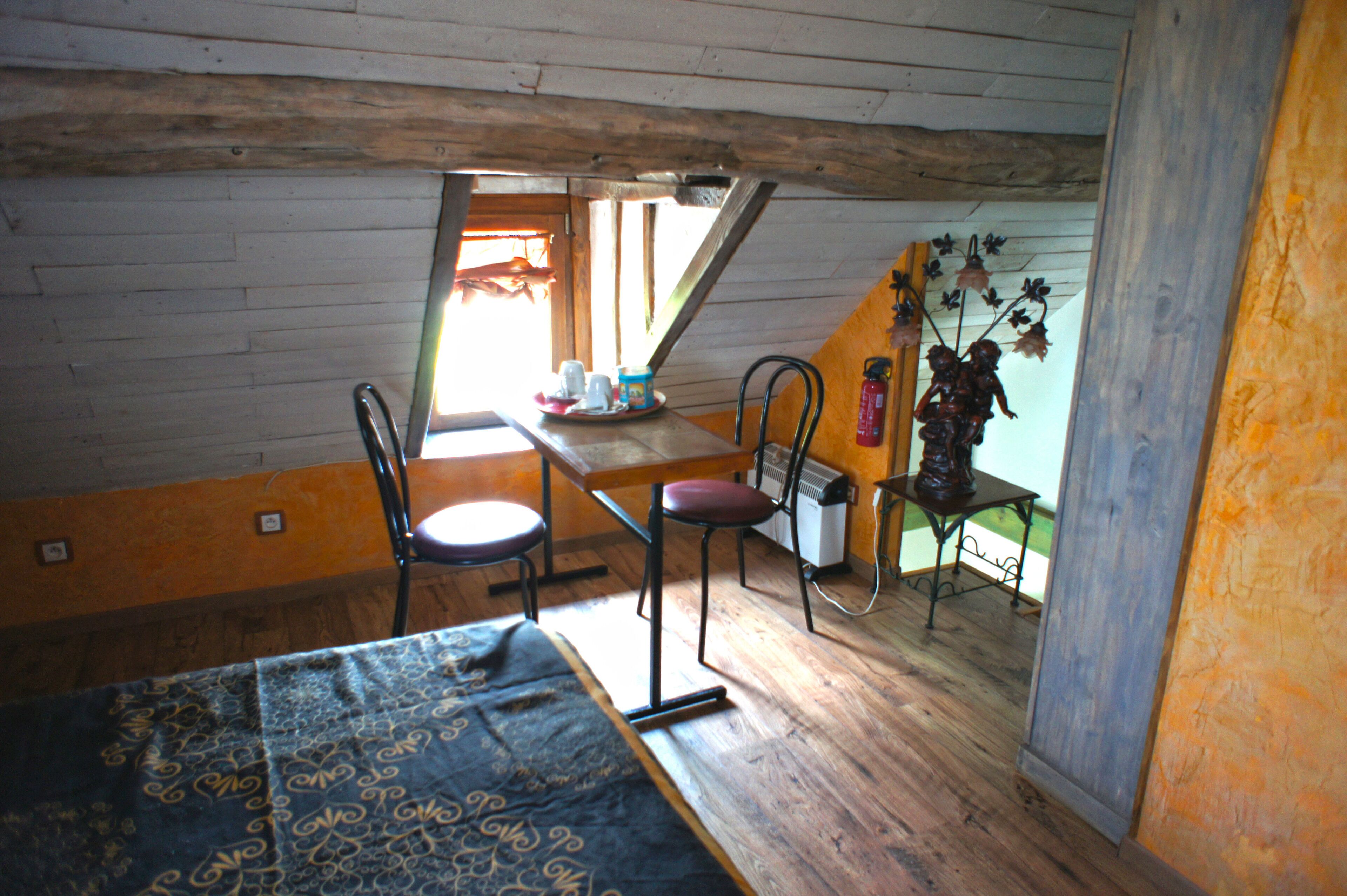 Una habitación con piso de madera, una cama, una mesa con sillas, un radiador y un ventanal con vistas al exterior.