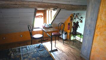 Una habitación con piso de madera, una cama, una mesa con sillas, un radiador y un ventanal con vistas al exterior.