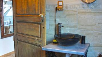 Une salle de bain avec une porte en bois, un lavabo avec un receveur, un miroir et un luminaire fixé au mur.