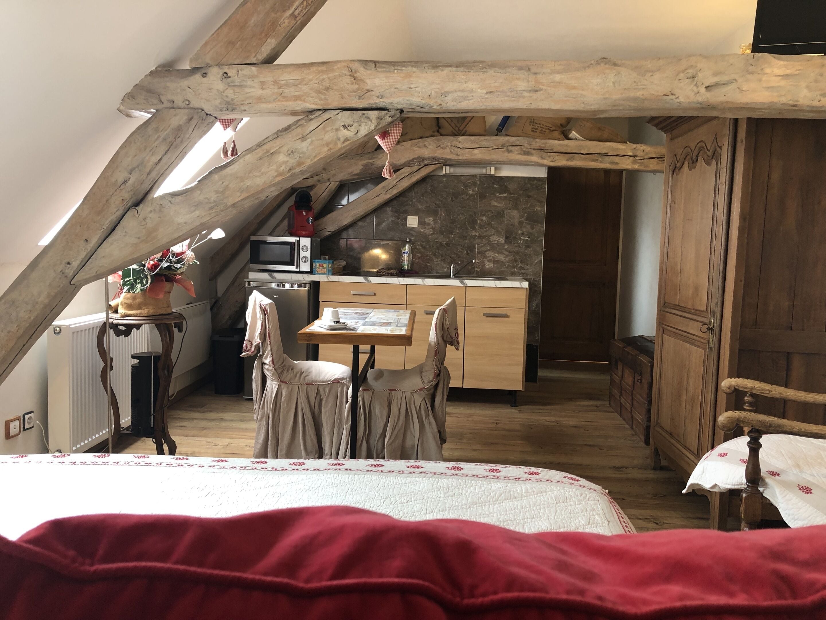 Ein gemütliches Schlafzimmer im Dachgeschoss mit einem Bett, einem kleinen Tisch und einem Stuhl. Es gibt eine Küchenzeile mit einer Mikrowelle, einem Spülbecken und Schränken. Der Raum verfügt über Holzbalken und eine geneigte Decke.