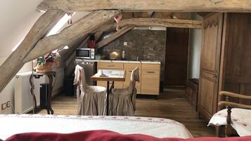 Ein gemütliches Schlafzimmer im Dachgeschoss mit einem Bett, einem kleinen Tisch und einem Stuhl. Es gibt eine Küchenzeile mit einer Mikrowelle, einem Spülbecken und Schränken. Der Raum verfügt über Holzbalken und eine geneigte Decke.